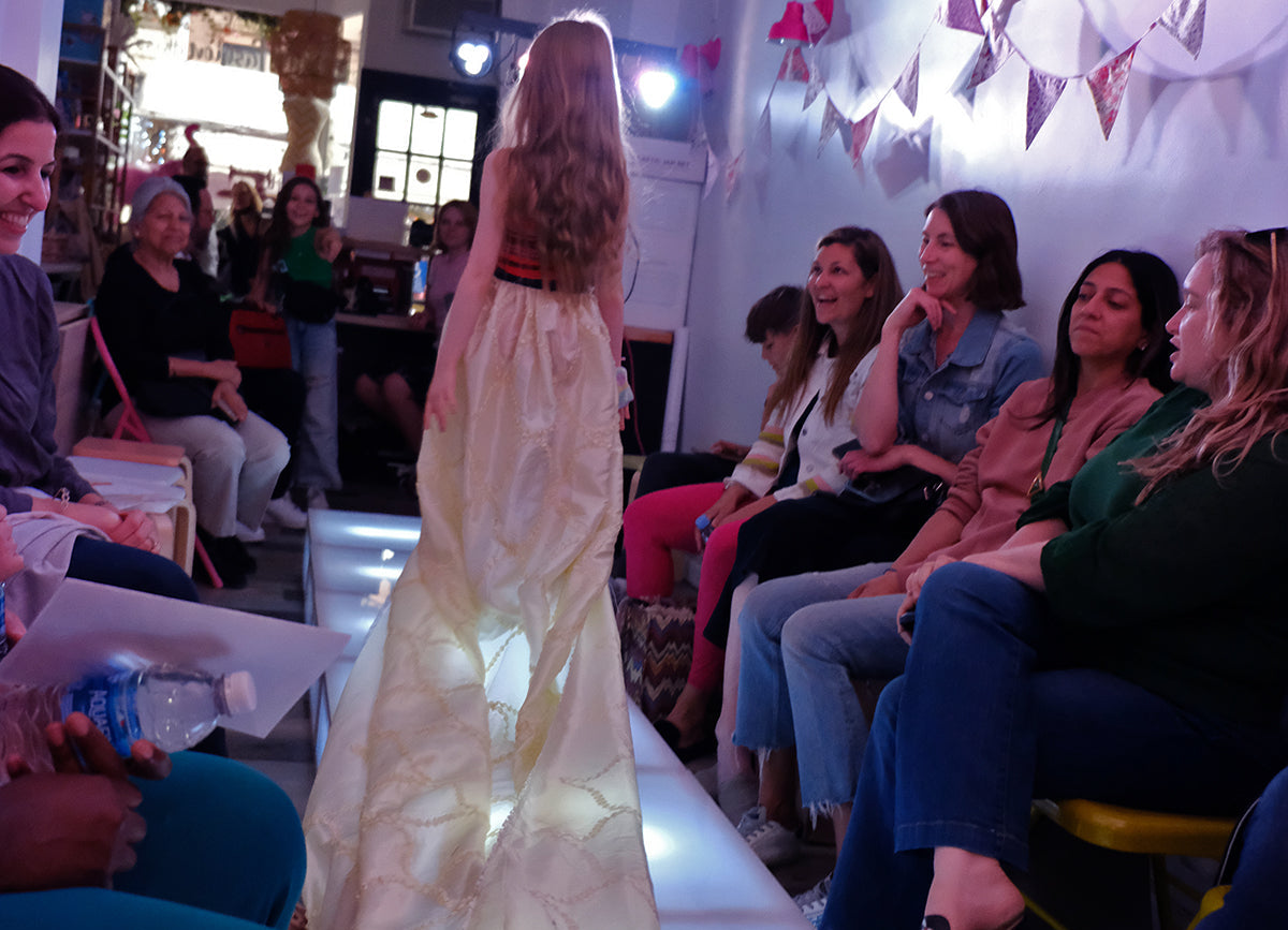 Woman in a long dress walking on a runway with an audience watching.