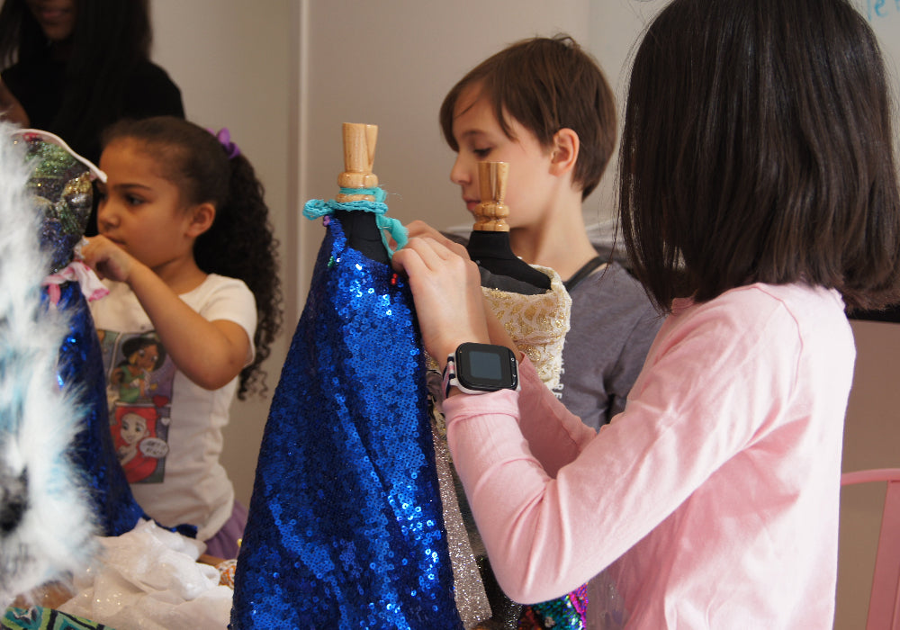 Children playing with a blue sequined dress and other items in a classroom setting.