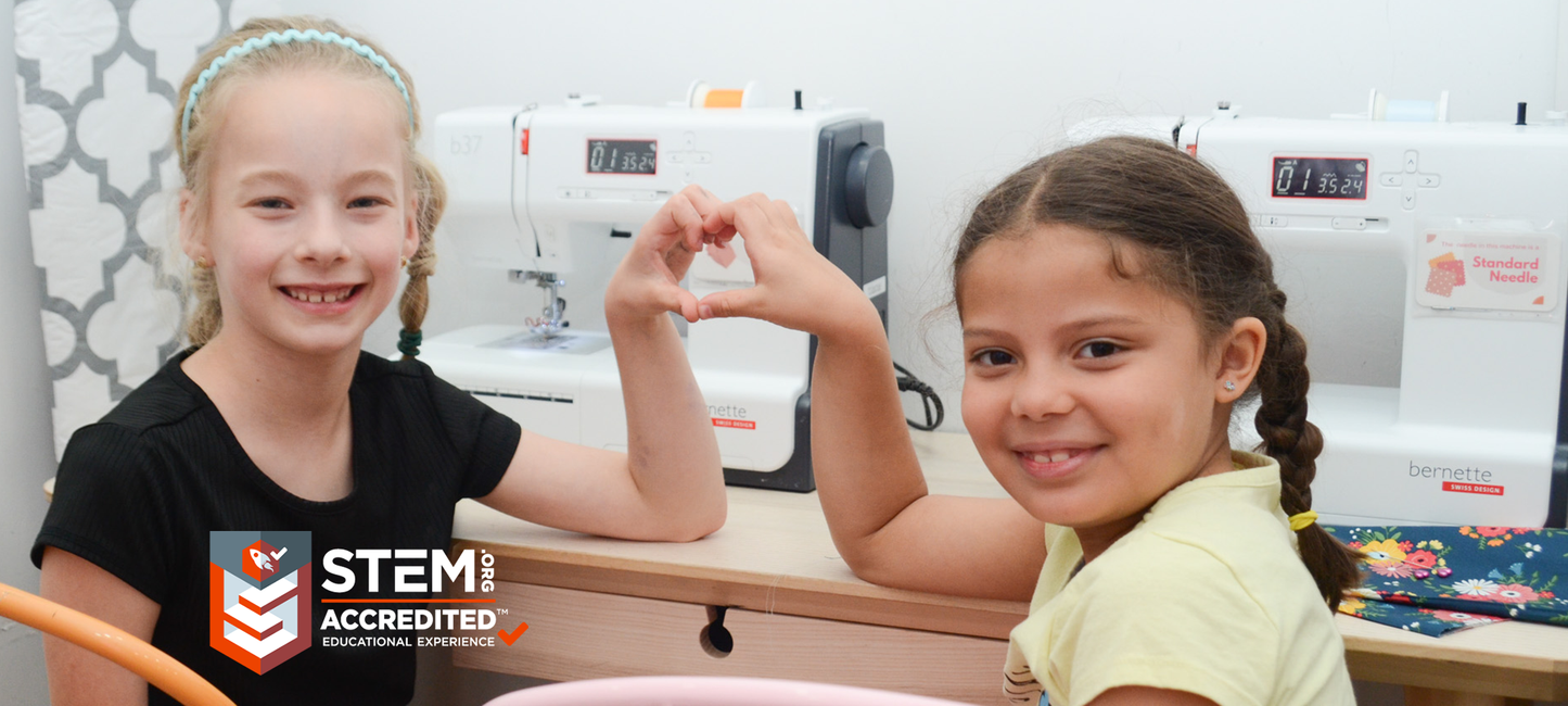 Two young girls in a classroom setting with sewing machines, STEM Accredited logo visible.