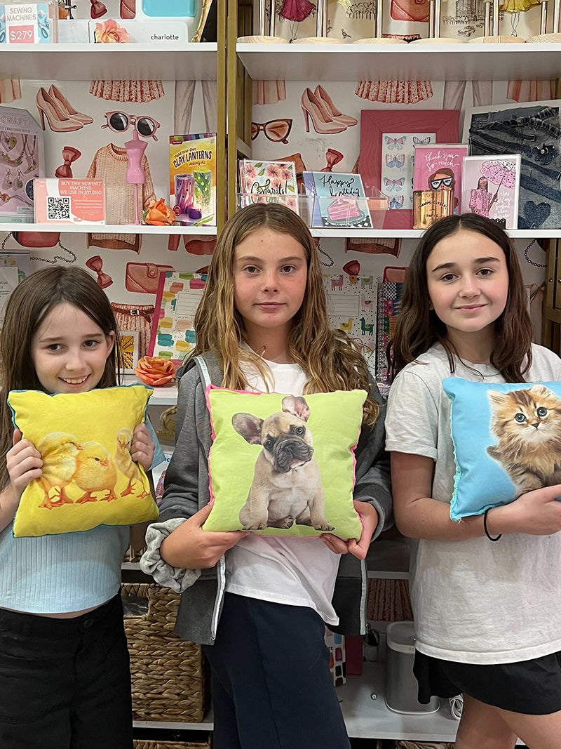 Three children holding colorful pillows with animal illustrations in a store setting.